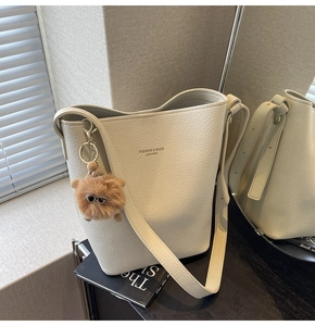 Detail of off-white lychee grain leather bucket bag with fashion lettering and plush charm