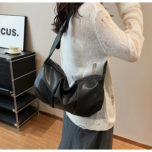 Close-up of a black pleated crescent shoulder bag with soft leather texture on a model