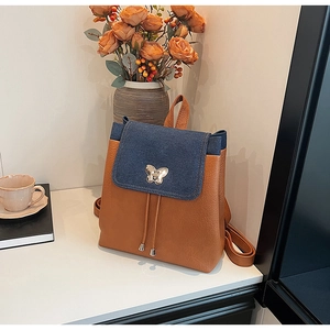 Detail of blue denim and brown leather patchwork backpack with silver butterfly buckle