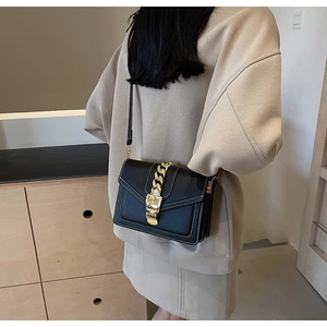 Detail of a black leather crossbody bag with bold gold chain and square metal clasp
