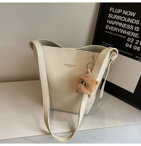 Detail of creamy white lychee leather bucket bag with golden logo and fuzzy monster charm
