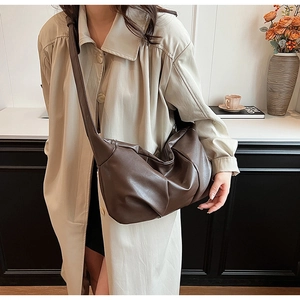 Detail of soft brown pleated croissant bag with wide shoulder strap worn with a trench coat