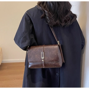 Detail of vintage brown crossbody bag with gold buckle on long trench coat