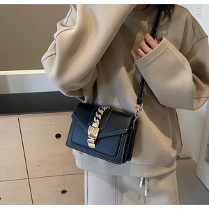 Detailed shot of black crossbody bag with bold gold chain and white stitching accents