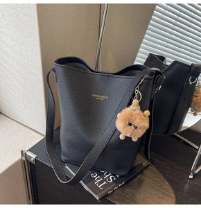 Detail of black pebbled leather bucket bag with gold lettering and brown plush charm