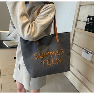 Détail du sac cabas en toile grise avec broderie orange et bandoulière en cuir