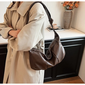Brown faux leather crescent bag with pleated design and knot detail worn by a model