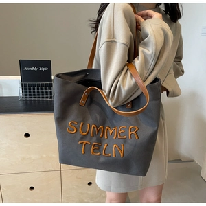 Détail du sac cabas en toile gris foncé avec poignées en cuir marron et broderies