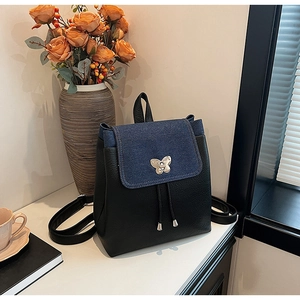Detail of a casual backpack with denim flap and silver butterfly clasp on wood table