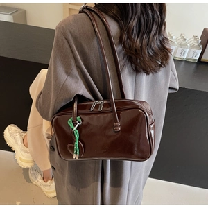 Détail d'un sac bandoulière en cuir verni marron foncé avec charm de coeur en cordon