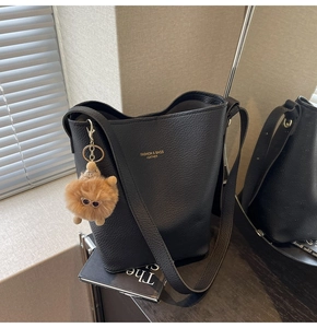 Detail of black lychee grain bucket bag with a cute brown plush doll pendant