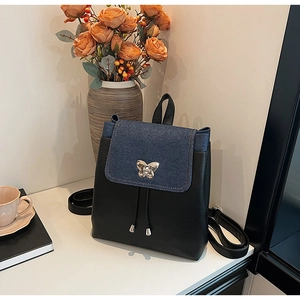 Detail of mini backpack featuring denim flap with butterfly buckle on white desk