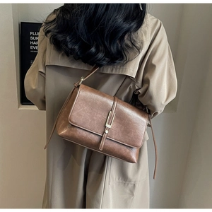 Detailed view of a vintage brown messenger bag paired with a classic khaki trench coat