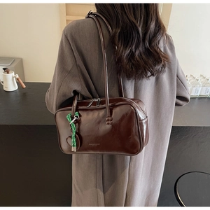 Détail du sac bowling en cuir marron brillant avec charm cœur porté à l'épaule