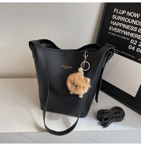 Detail of black pebbled leather bucket bag with gold lettering and plush charm