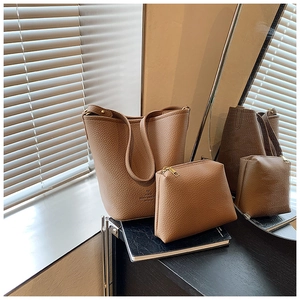 Brown lychee leather bucket bag and pouch set on a desk with soft natural light