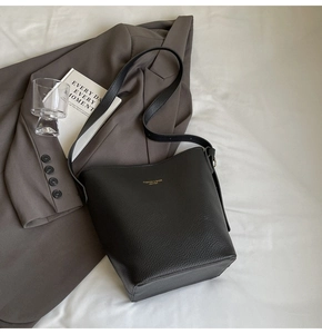 Close-up of black lychee grain leather bucket bag with gold lettering on white fabric