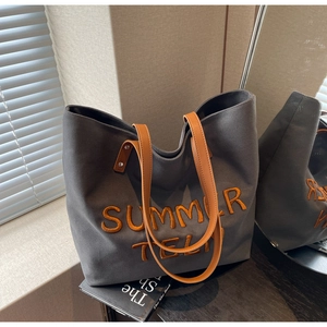 Détail du sac cabas en toile grise avec broderie orange et poignées en cuir marron