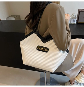 Detail of a pleated tote bag with black trim and golden Fashion logo on white fabric