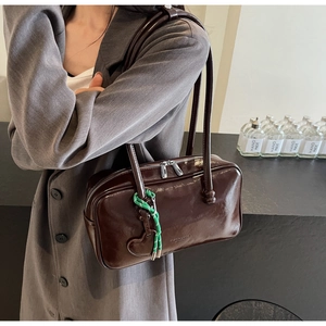Détail du sac à main en cuir verni marron foncé avec charm cœur et cordon tressé vert