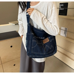 Detail der dunkelblauen Denim-Umhängetasche mit Kontrastnähten und Buchstaben-Druck