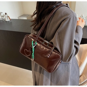 Détail du sac bowling en cuir brillant marron foncé avec breloque cœur et cordon tissé