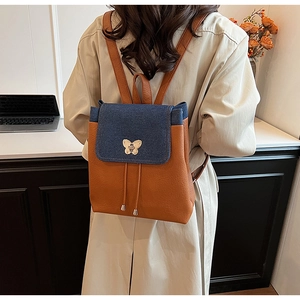 Detail of a brown leather backpack with denim flap and gold butterfly clasp on model