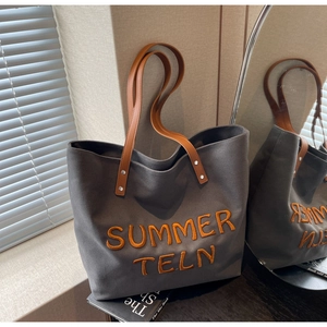 Détail du sac cabas en toile grise avec broderie orange et anses en cuir marron