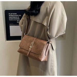 Brown vintage faux leather crossbody bag with metal lock shown on a beige trench coat