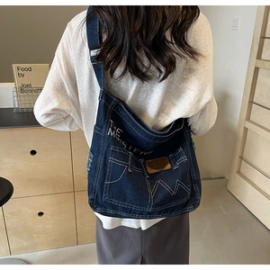Detail der dunkelblauen Denim-Umhängetasche mit weißen Nähten und Leder-Markenetikett
