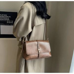 Detail of vintage brown PU leather crossbody bag with metallic buckle on a beige coat