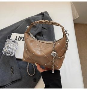 Detail of khaki quilted handbag with silver studs and elegant chain handle on grey fabric