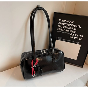 Détail d'un sac à épaule en cuir noir brillant avec un pendentif coeur rouge tressé