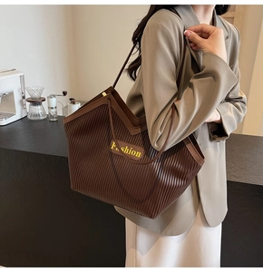 Detailed view of brown pleated tote bag featuring a vertical texture and Fashion label