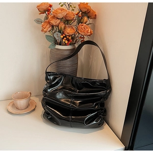 Detail of black glossy patent leather shoulder bag with stylish pleats and soft hobo shape