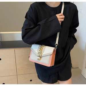 Detail view of contrast color crossbody bag with gold chain and metal buckle on model