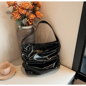 Detail of black glossy pleated shoulder bag with metallic logo in a lifestyle setting