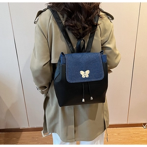 Detail of a color-block backpack with denim flap and silver butterfly lock on back of a model