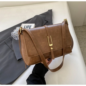 Detail of vintage brown shoulder bag with gold metal U-lock on white textured surface