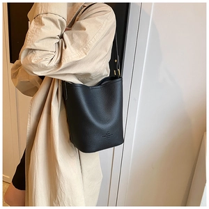 Detail of black lychee grain leather bucket bag with a logo on an adjustable strap