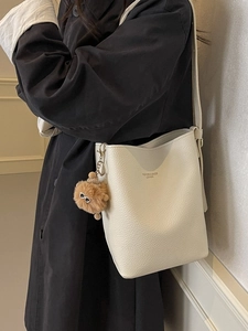 Off-white lychee leather bucket bag with plush bear charm and adjustable shoulder strap