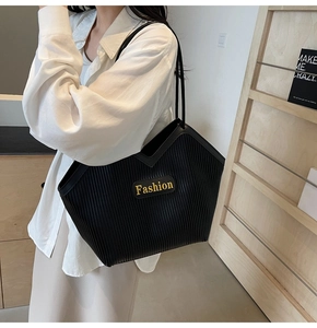 Close-up of black tote bag with vertical pleats and golden Fashion logo on model