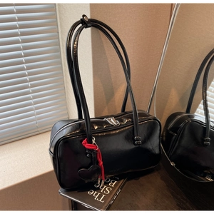 Détail du sac bowling noir verni brillant avec pendentif cœur rouge sur un livre
