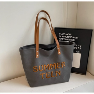 Détail du sac cabas en toile grise avec broderie orange et bandoulières en cuir