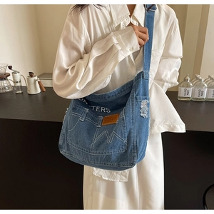 Detail der blauen Denim-Umhängetasche mit weißem TERS-Schriftzug und Tasche mit Fransen