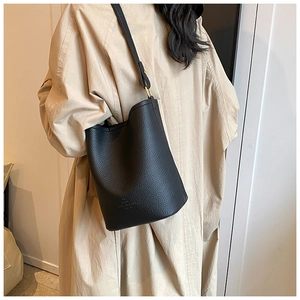Detailed shot of black lychee grain leather bucket bag worn with a stylish trench coat