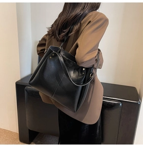Vue détaillée d'un grand sac cabas en cuir noir brillant porté avec une veste vintage