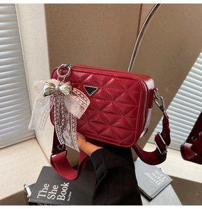 Detail of red quilted leather camera bag with wide strap and silver bow charm