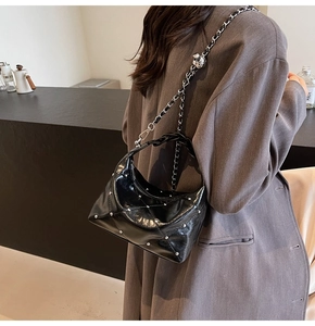 Detail of black quilted hobo bag with silver studs and chain strap worn by a model