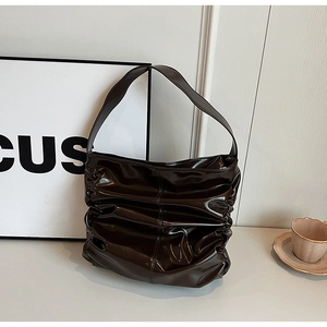 Detailed close-up of glossy brown faux leather shoulder bag with horizontal pleats